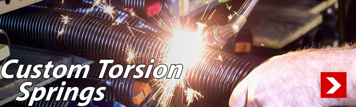 Custom torsion springs image with a hand holding a torsion spring and a torch cutting the springs. 